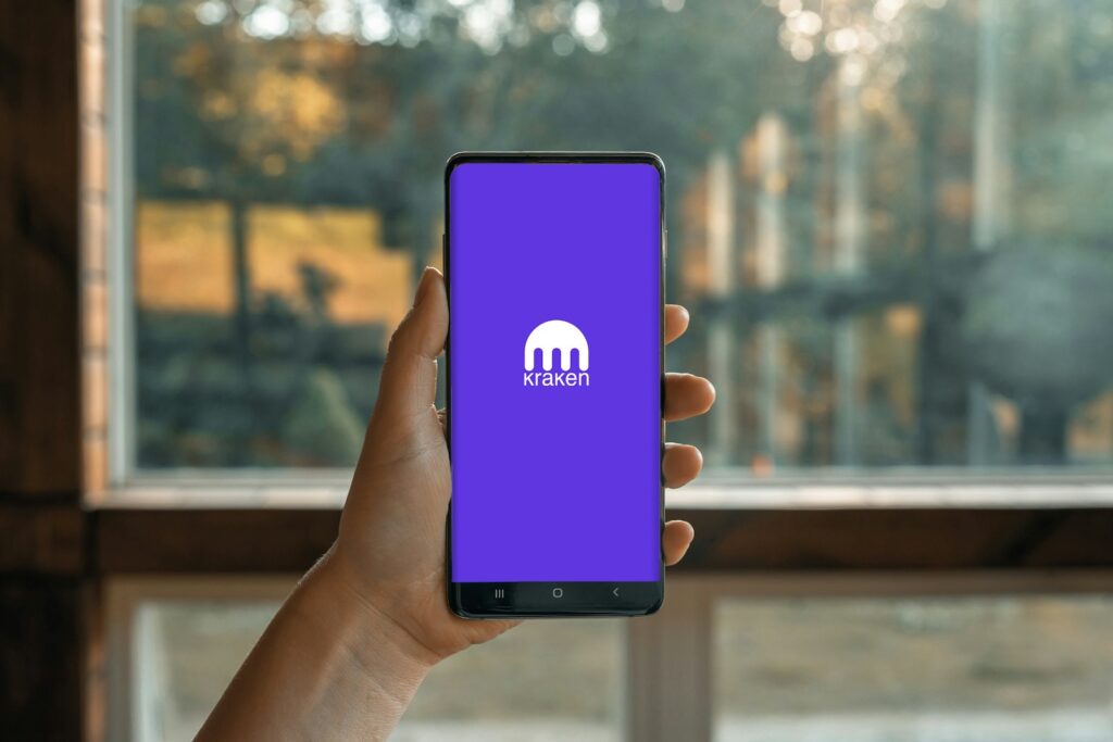 a hand holding a cell phone showing kraken cryptocurrency app